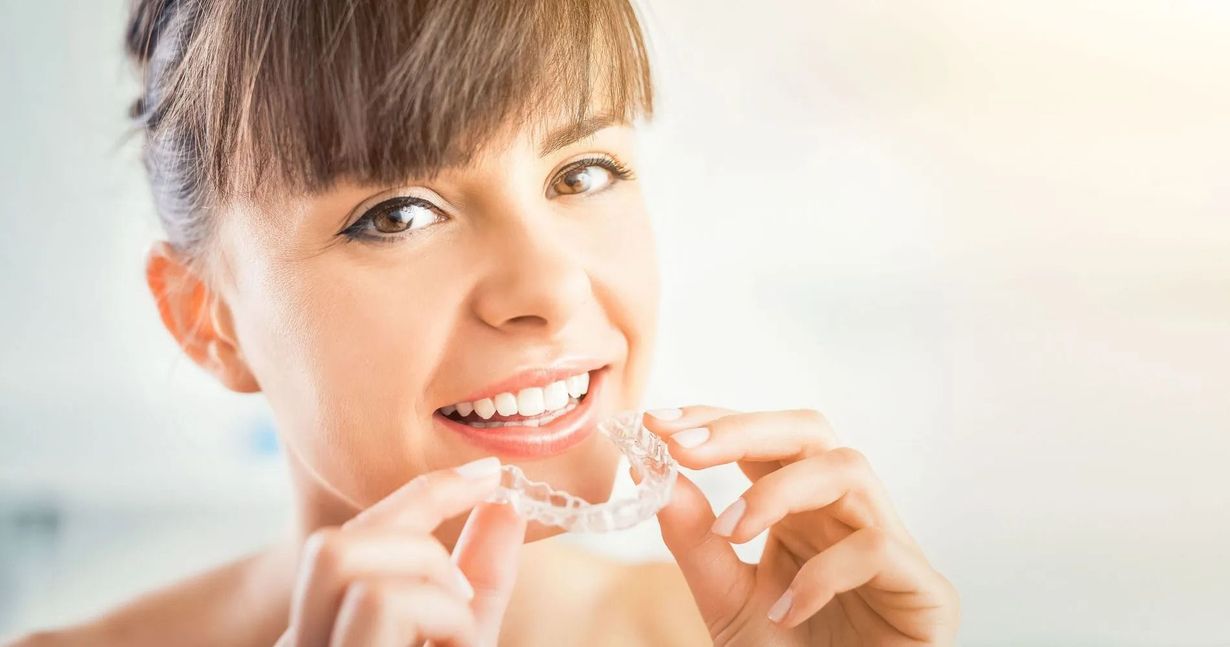 Woman smiling, holding clear dental aligners near her teeth.