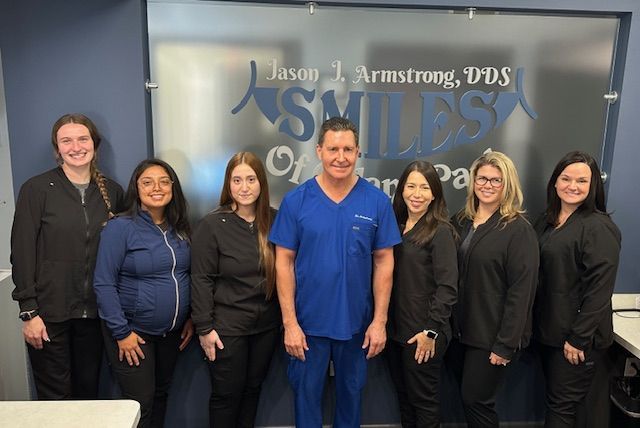Group of dental staff in front of frosted glass with logo, Jason J. Armstrong, DDS, Smiles of Upper Park.