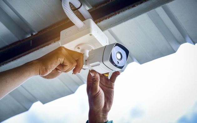 Person installing a security camera under a white roof.