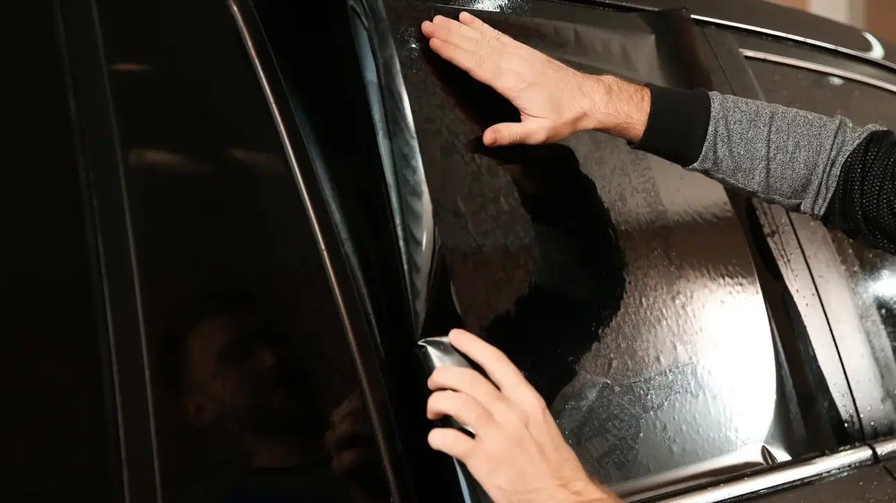 Hands handling a shiny black car door or window at night