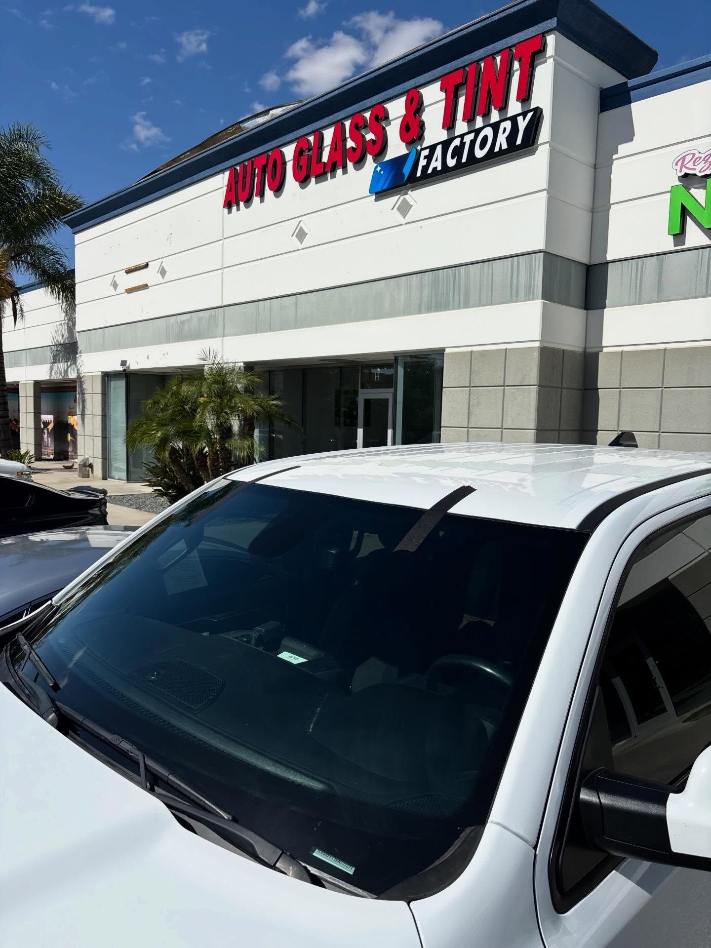 Windshield in front of a glass tint shop with a white and gray storefront under a sunny blue sky
