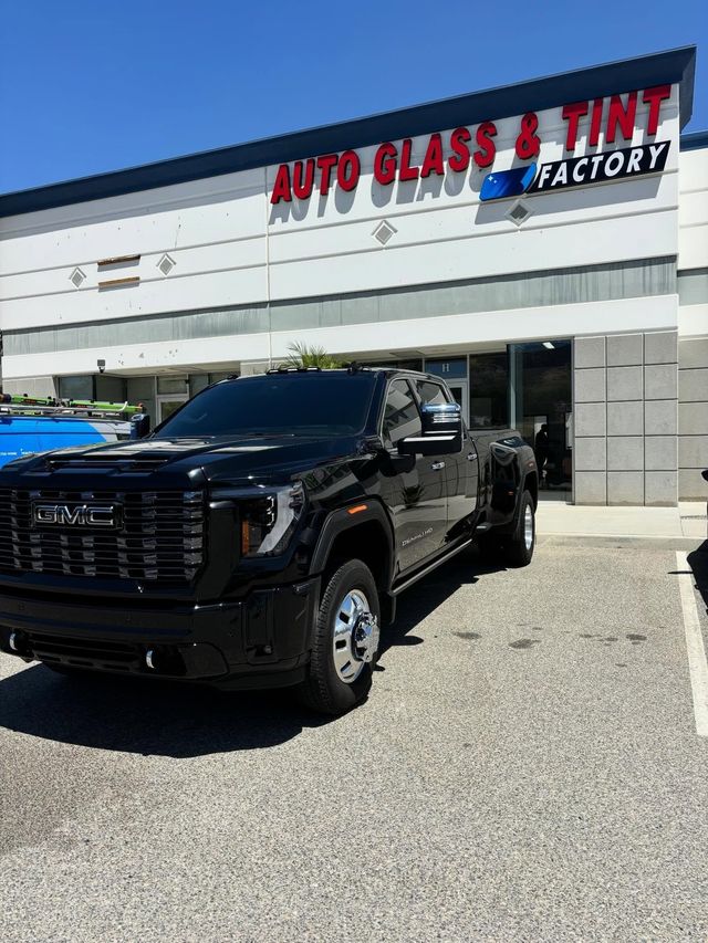 Black pickup truck parked outside Auto Glass & Tint Factory storefront in bright sunlight