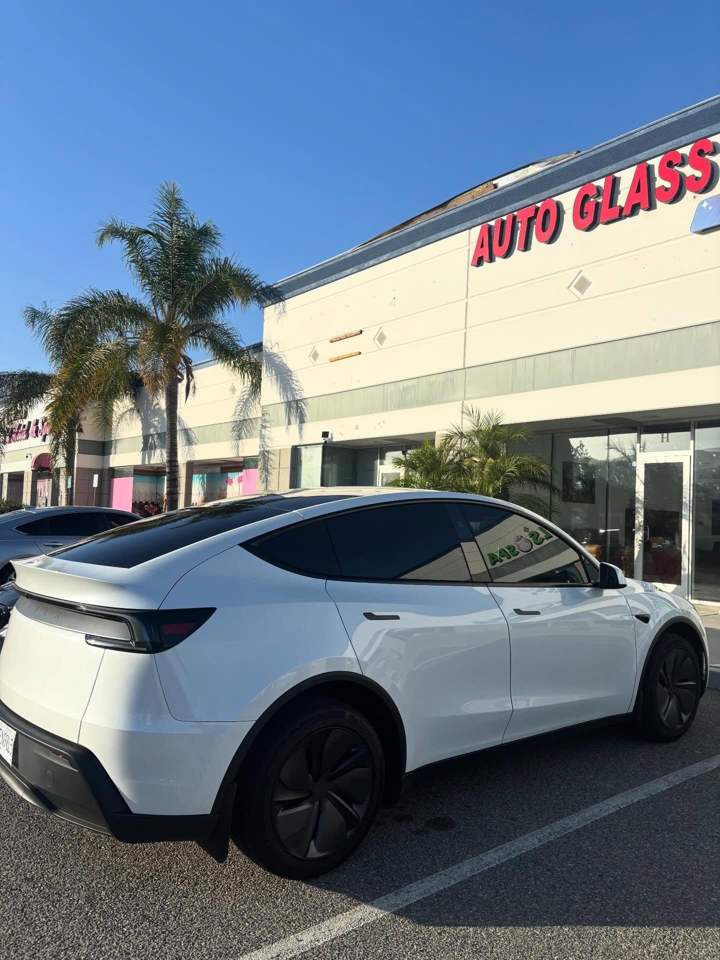 White Tesla parked outside an auto glass shop under a clear blue sky
