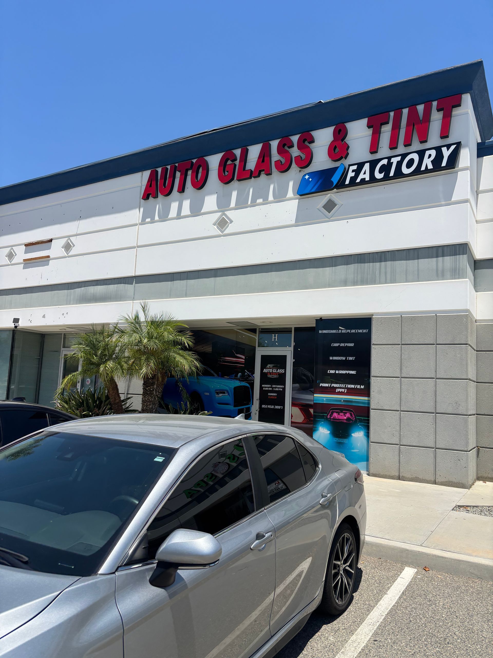Silver car parked outside Auto Glass & Tint Factory storefront on a sunny day