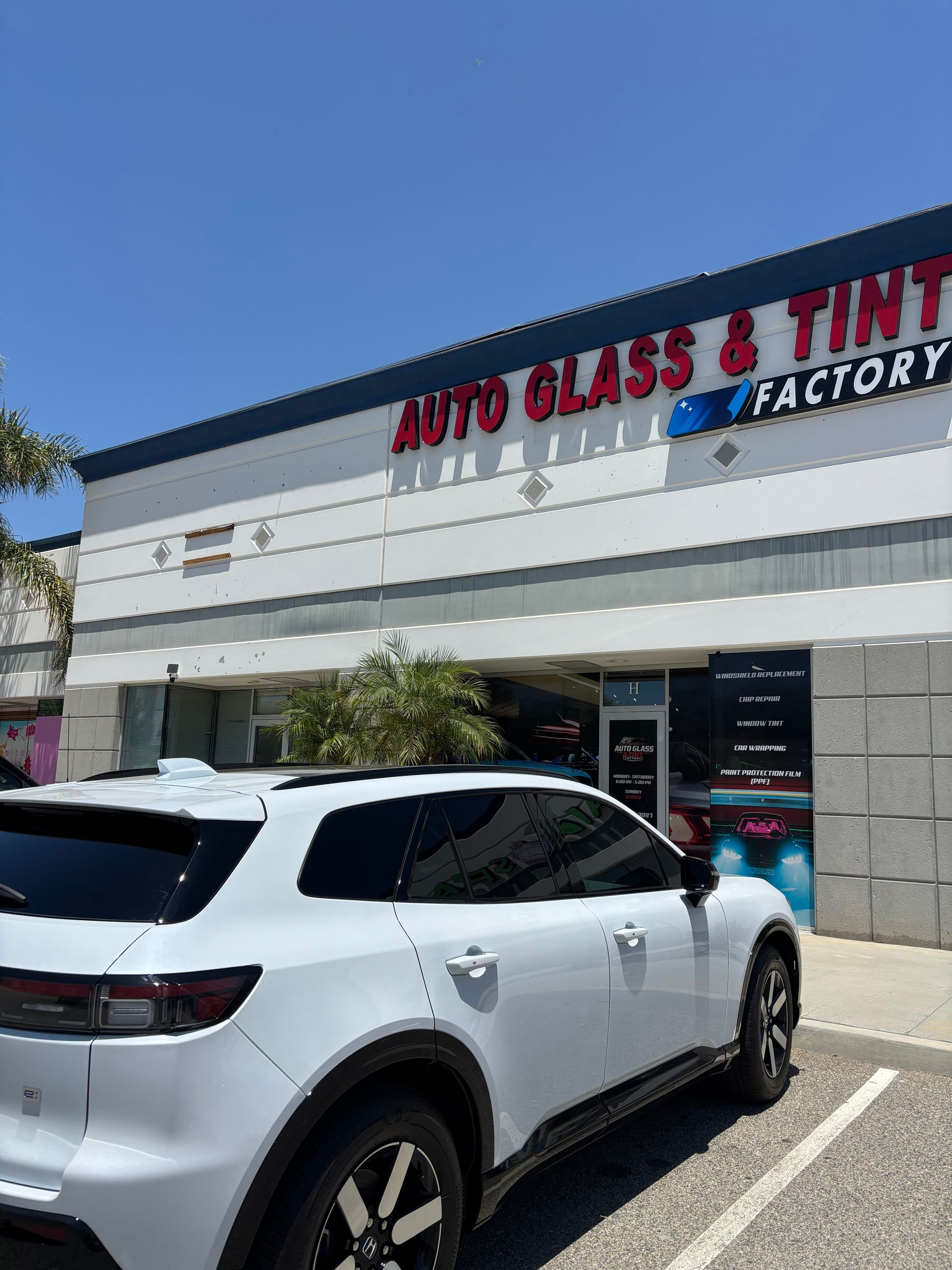 White SUV parked outside an auto glass and tint shop under a clear blue sky