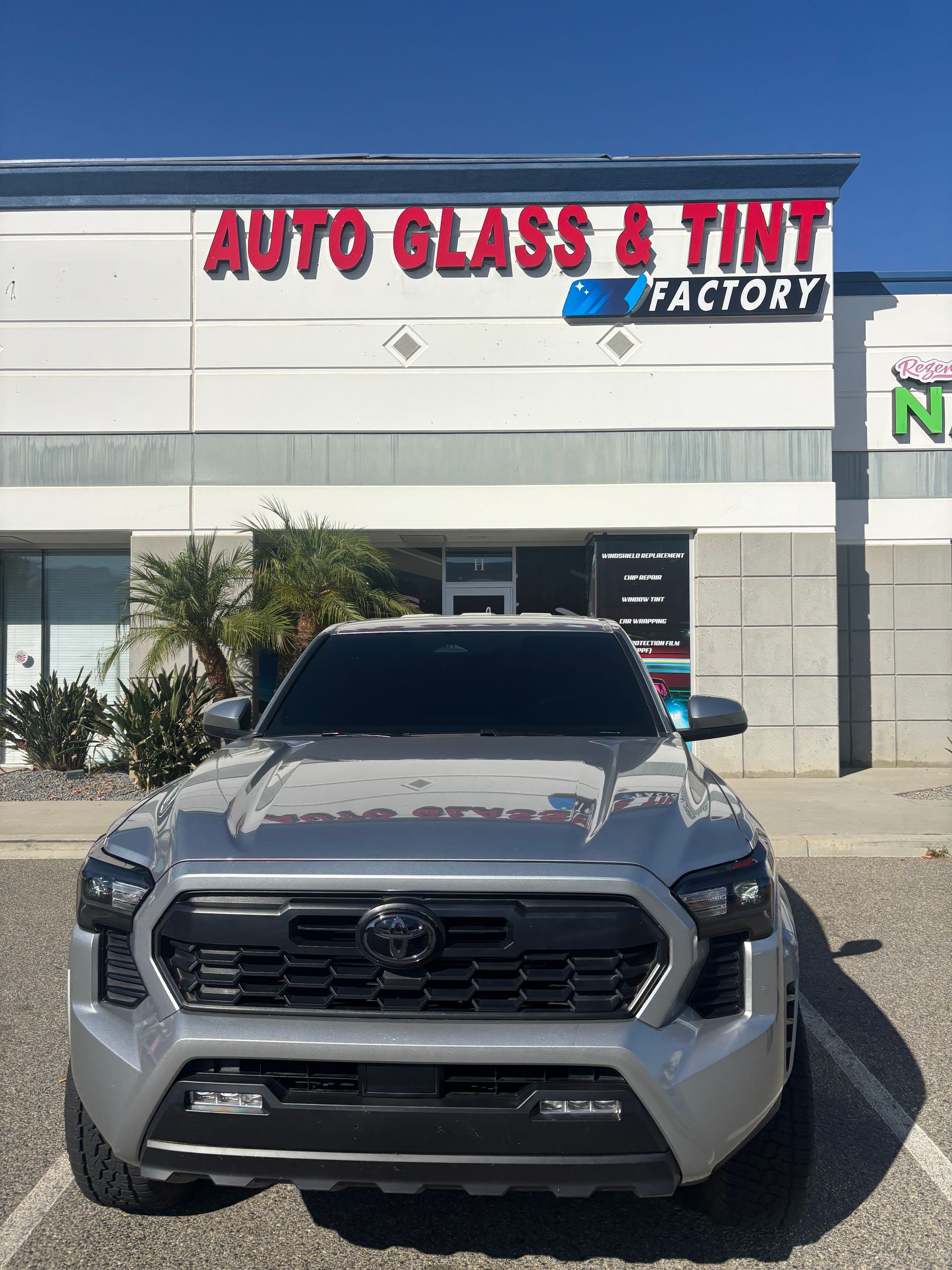 Gray pickup truck parked in front of Auto Glass & Tint Factory storefront
