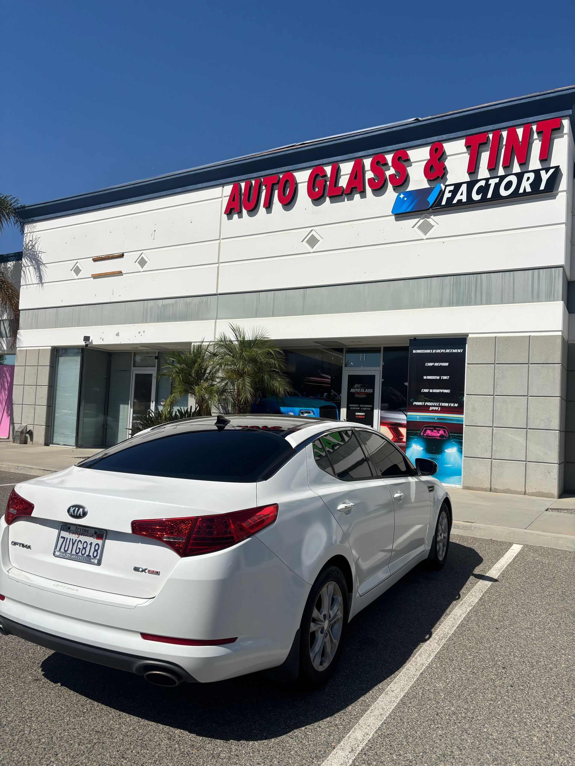 White sedan parked outside Auto Glass & Tint Factory storefront under red and blue signage