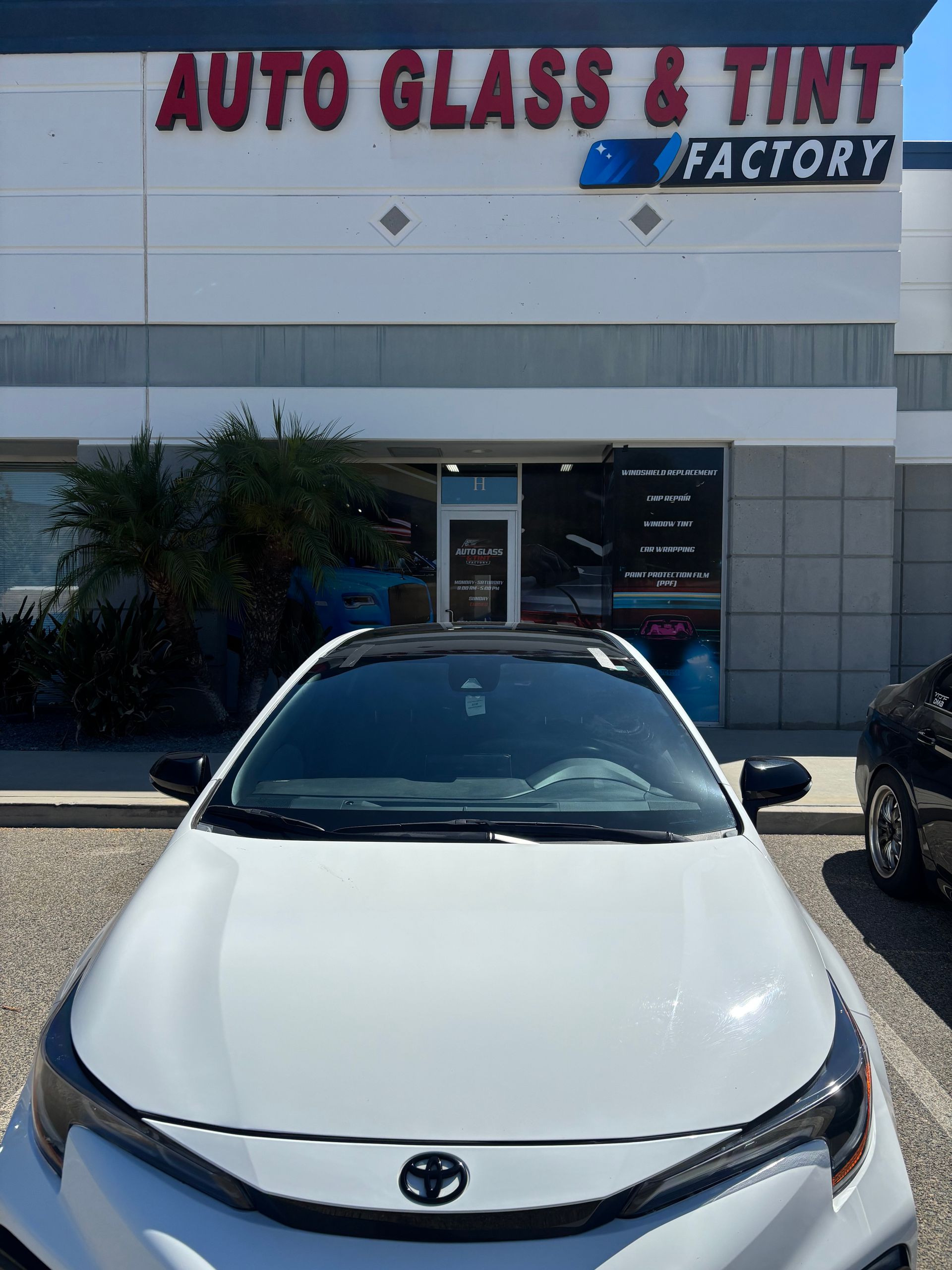 White Toyota parked in front of an Auto Glass & Tint Factory storefront