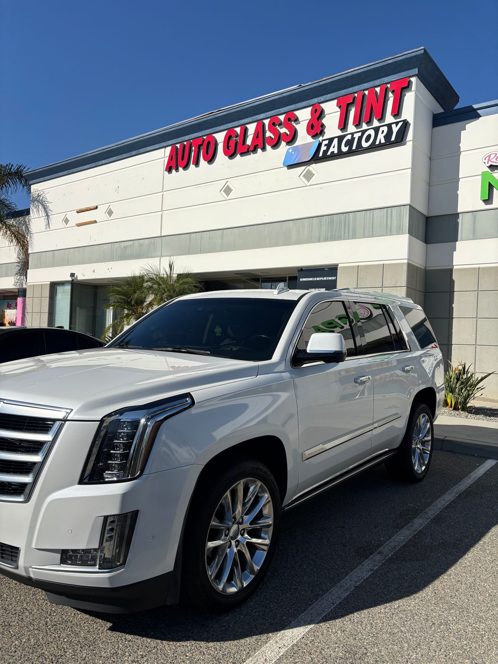 Silver SUV parked outside a storefront with a red “Auto Glass & Tint Factory” sign.