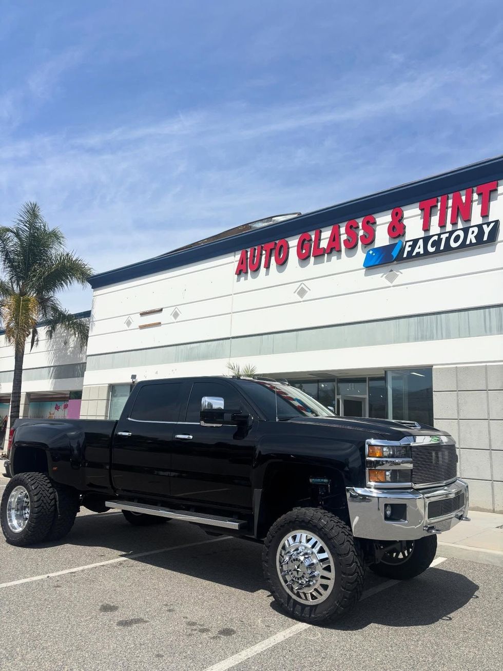 Black lifted pickup truck parked outside Auto Glass & Tint factory building