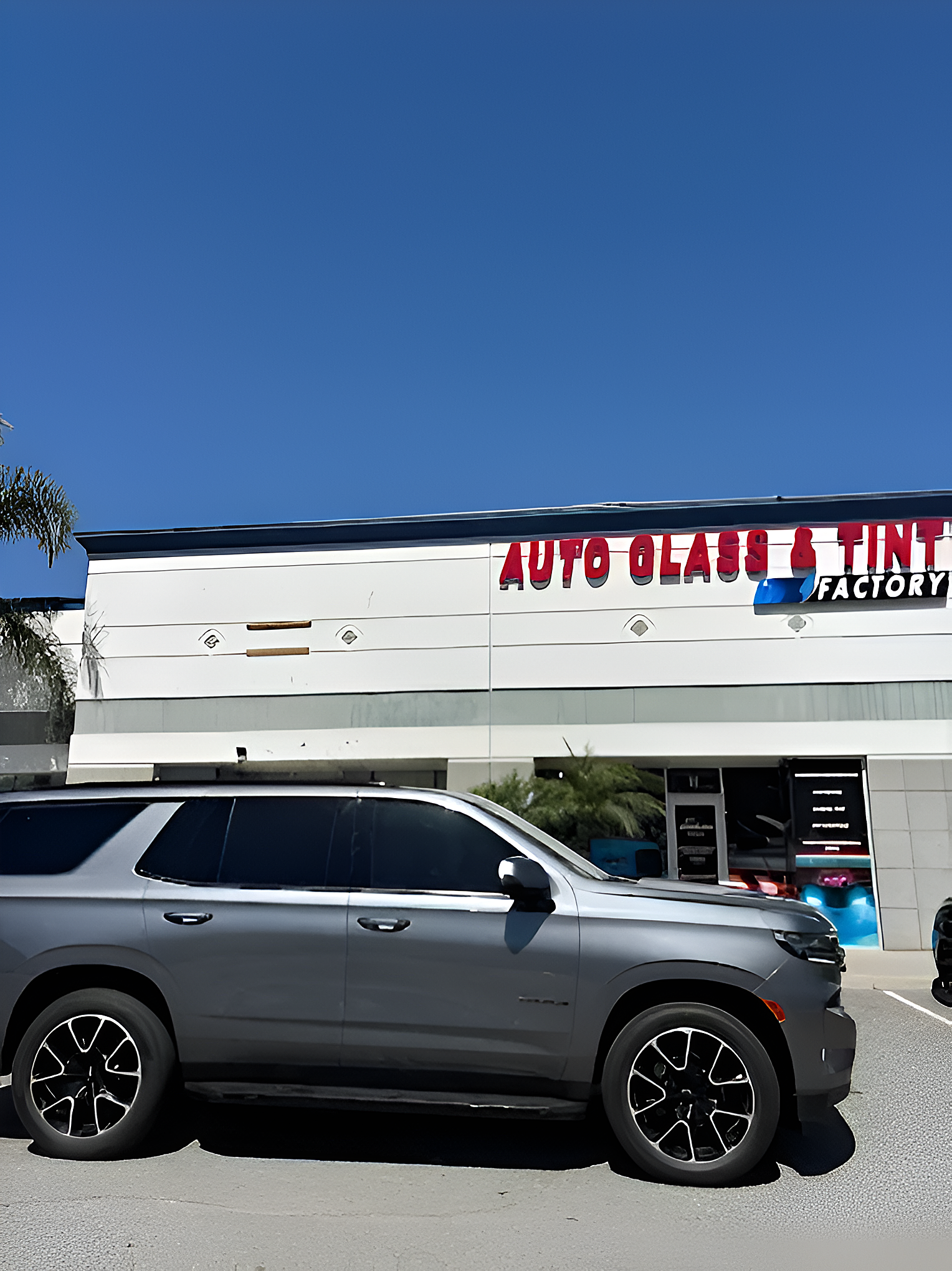 Gray SUV parked outside Auto Glass & Tint Factory storefront under a clear blue sky