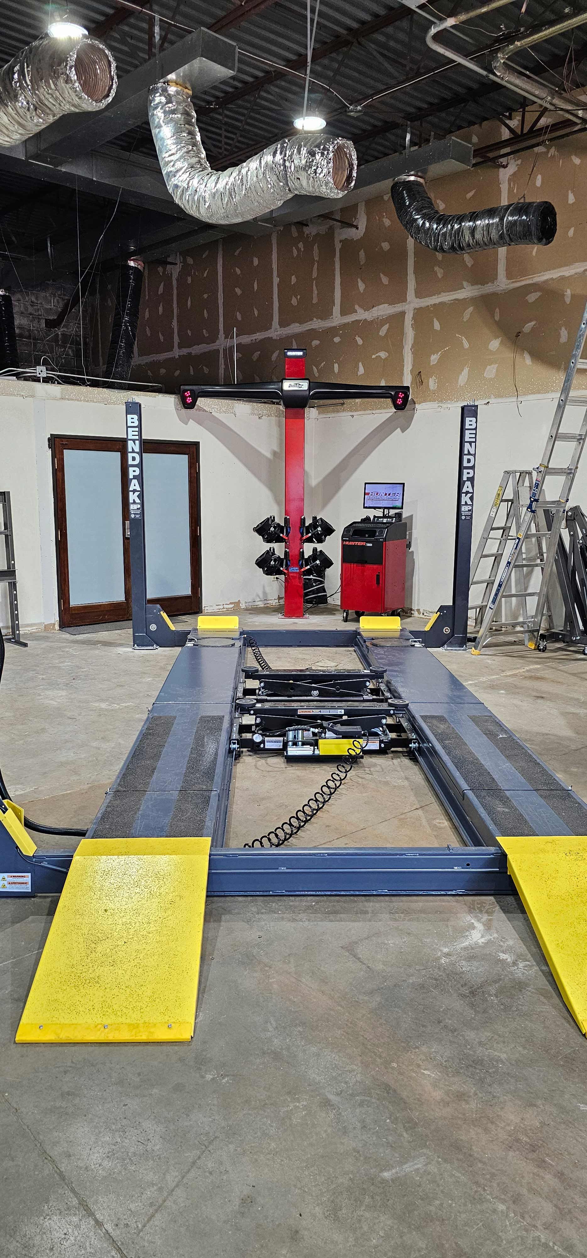 Indoor automotive workshop with a car lift, yellow ramps, and tools under exposed ductwork