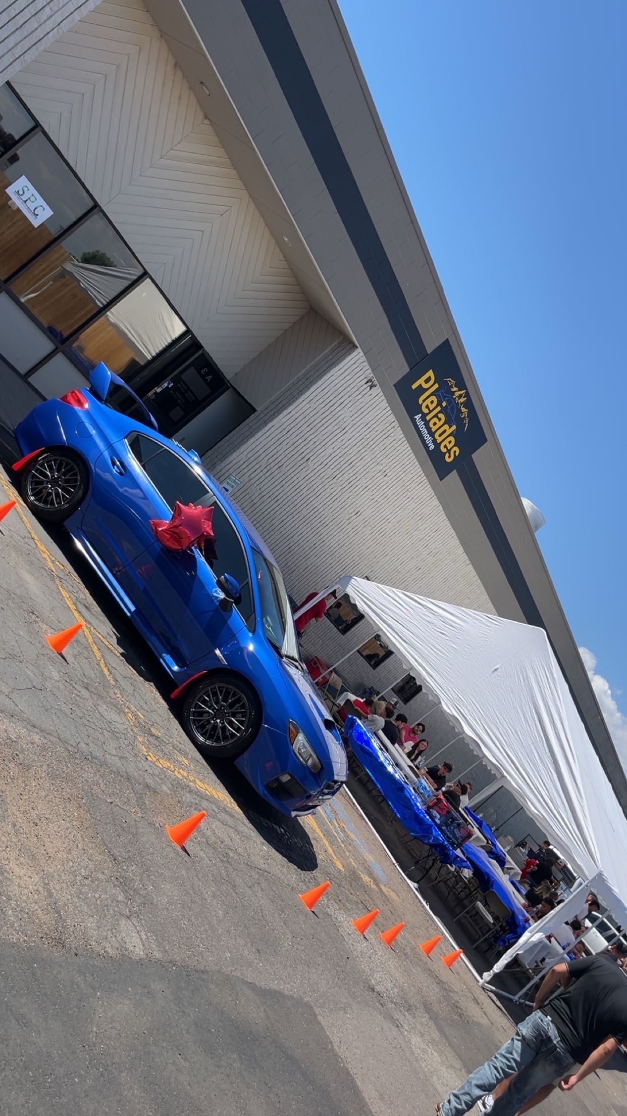 Blue sports cars parked outside a dealership under an awning with orange cones nearby