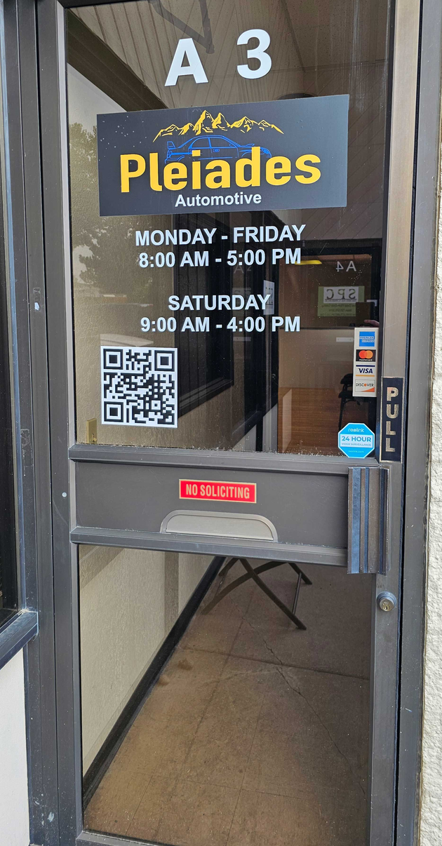 Front door to Pleiades with business hours on a glass panel and a QR code sign below