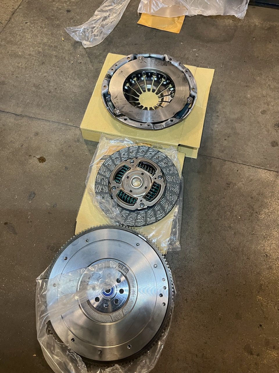Three metal clutch components arranged on a floor, including a large silver disc at the bottom.