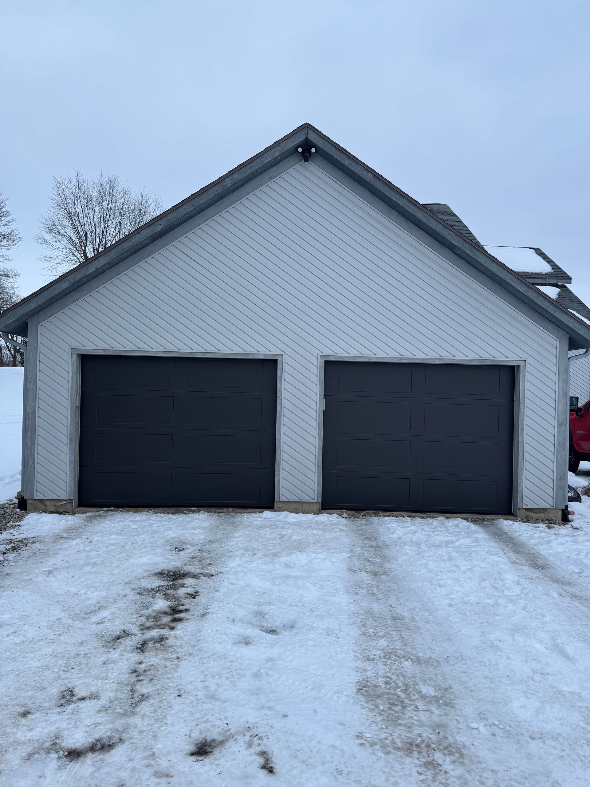 A white garage with black garage doors is covered in snow.