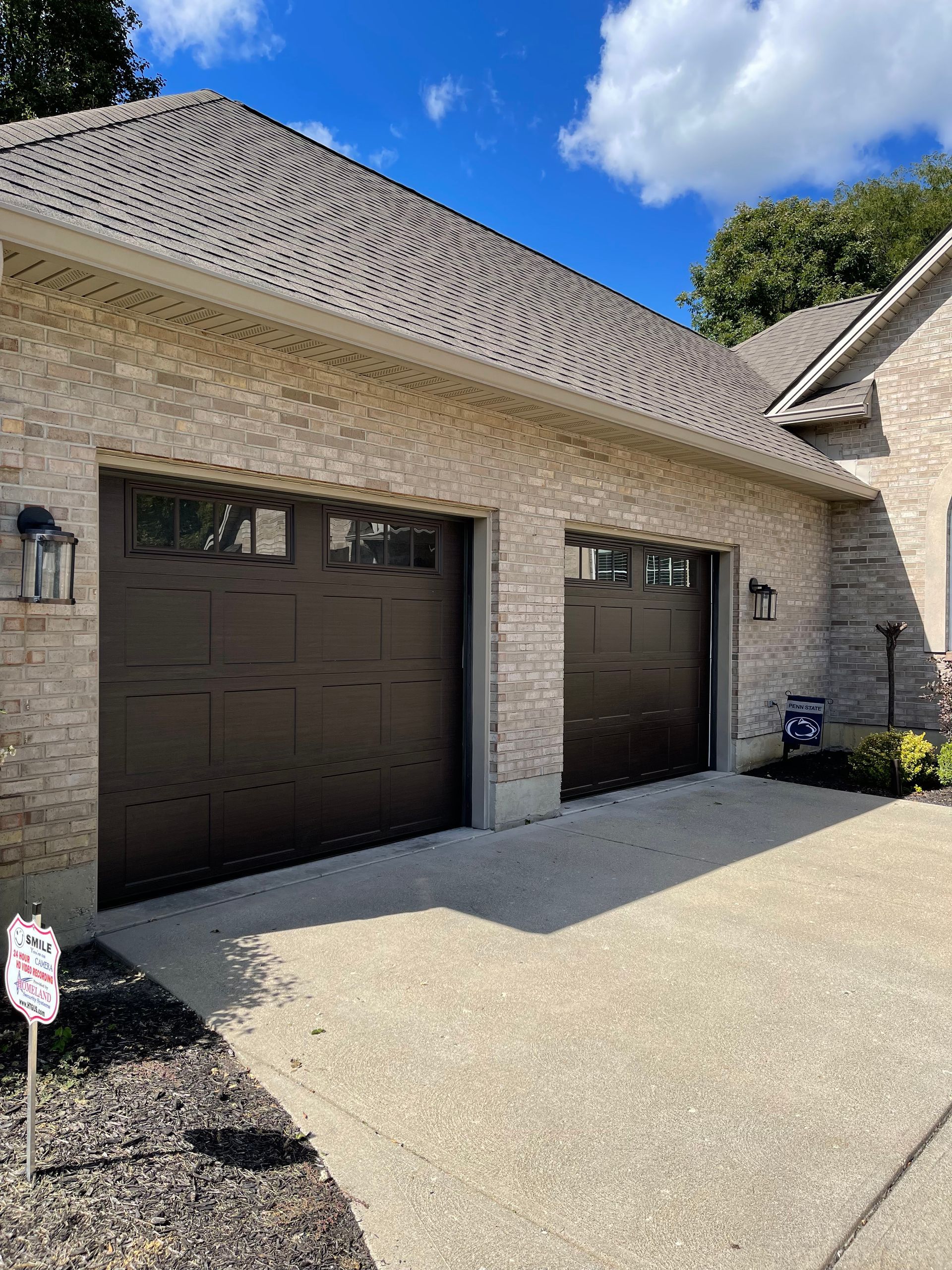 There are two garage doors on the side of a brick house.