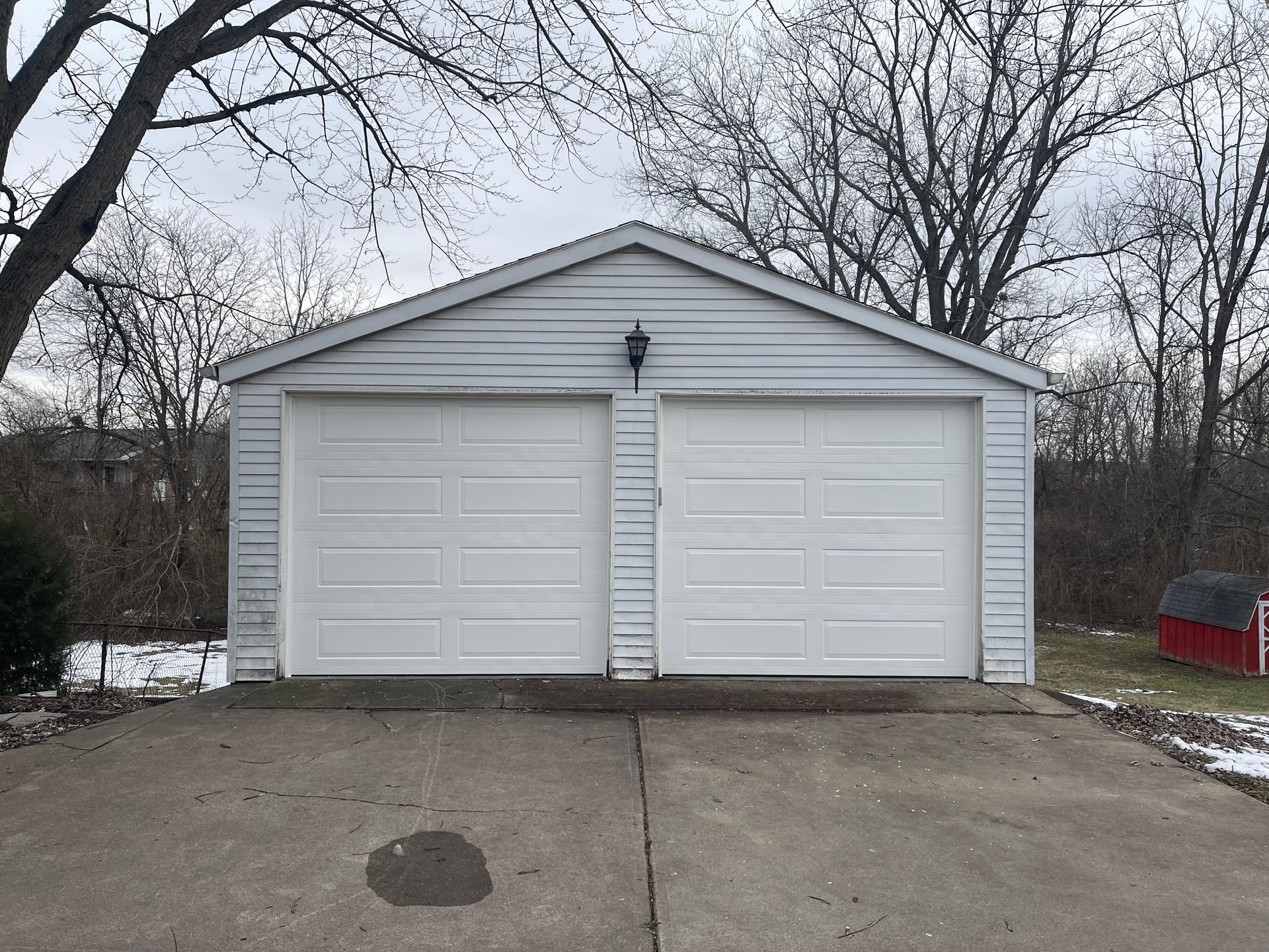 A white garage with two garage doors and a red barn in the background.