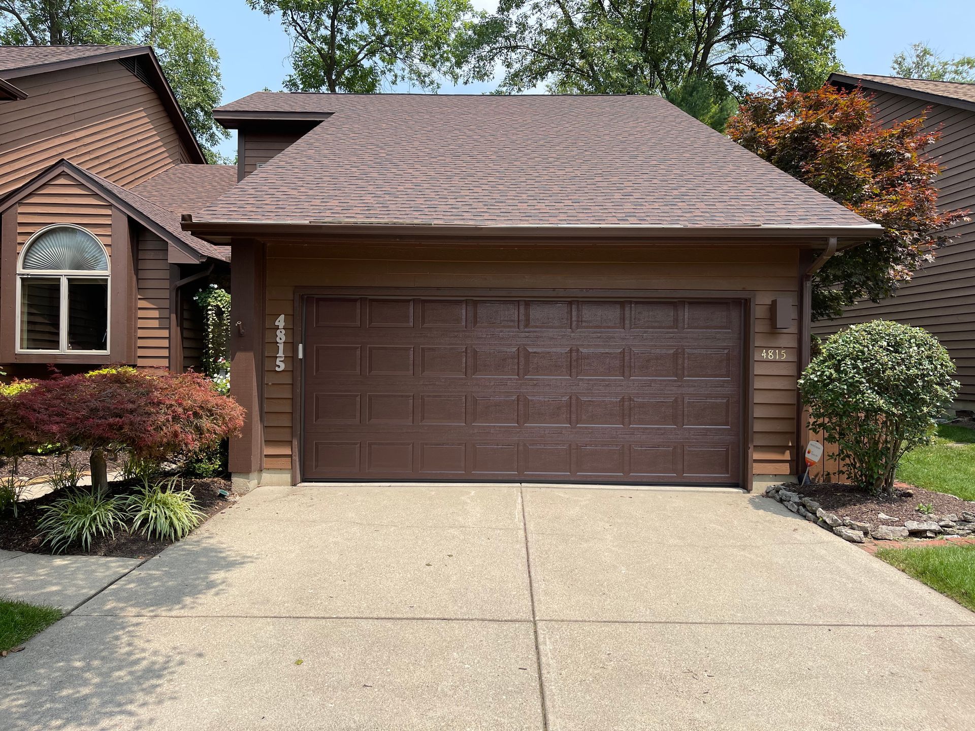 A brown garage door is sitting in front of a house.