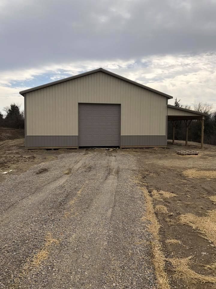 A large metal building with a garage door is sitting on top of a gravel road.