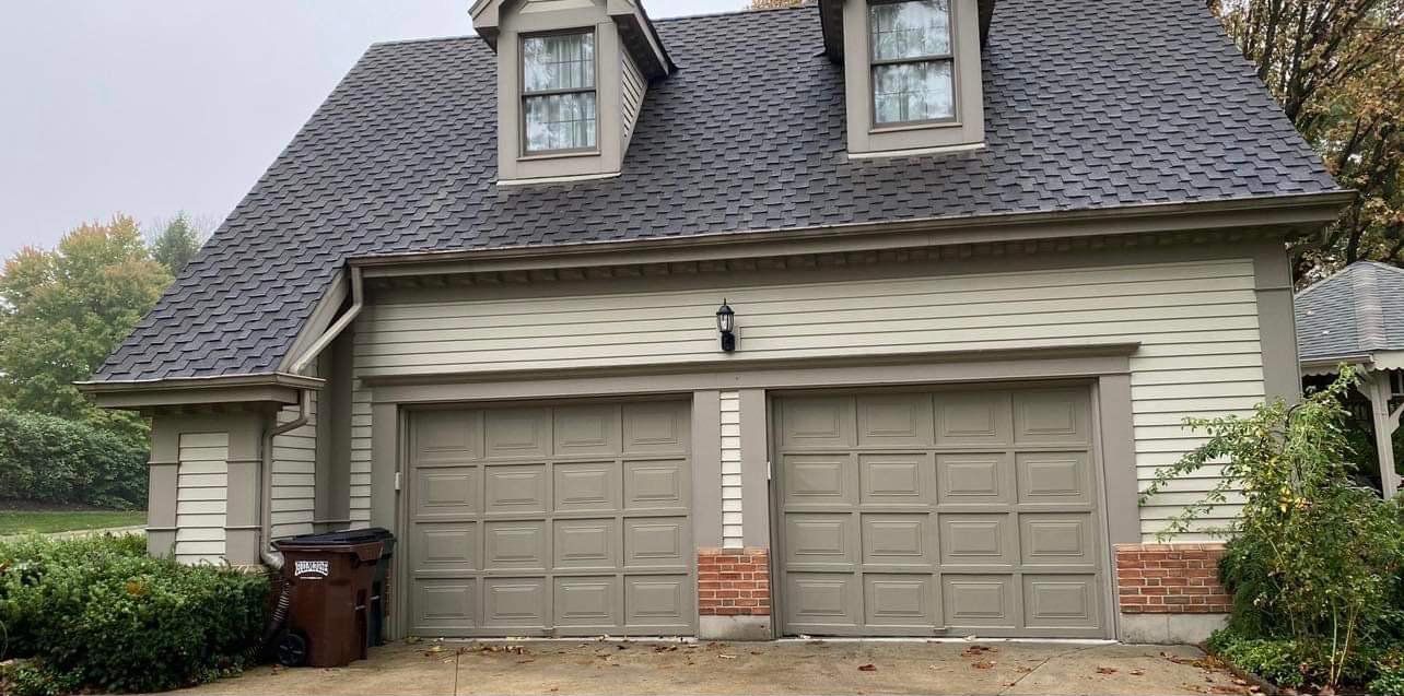 A house with a garage and a trash can in front of it.