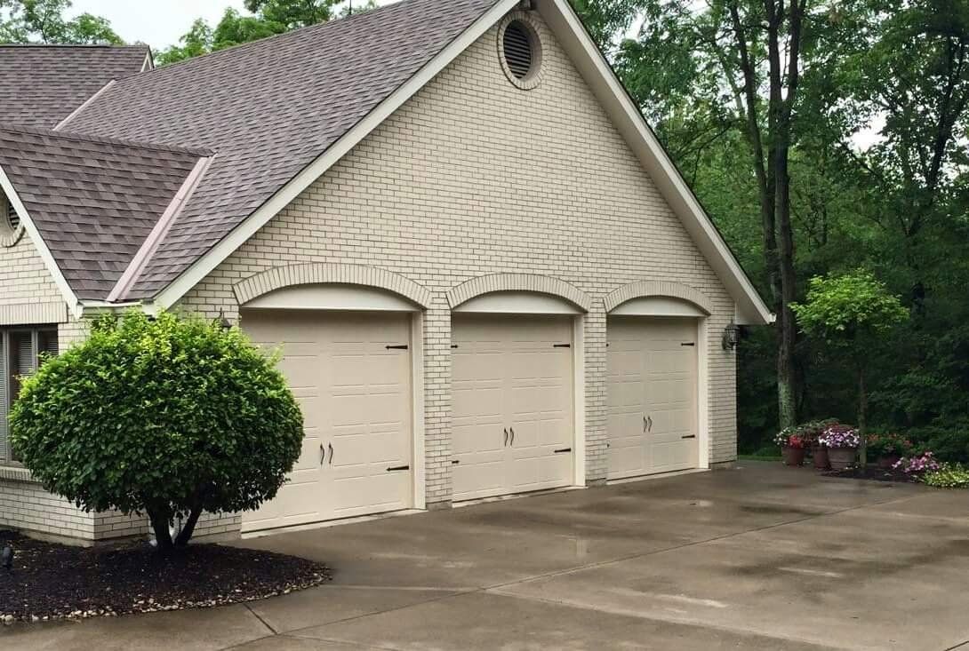 A large white brick house with three garage doors and a driveway.
