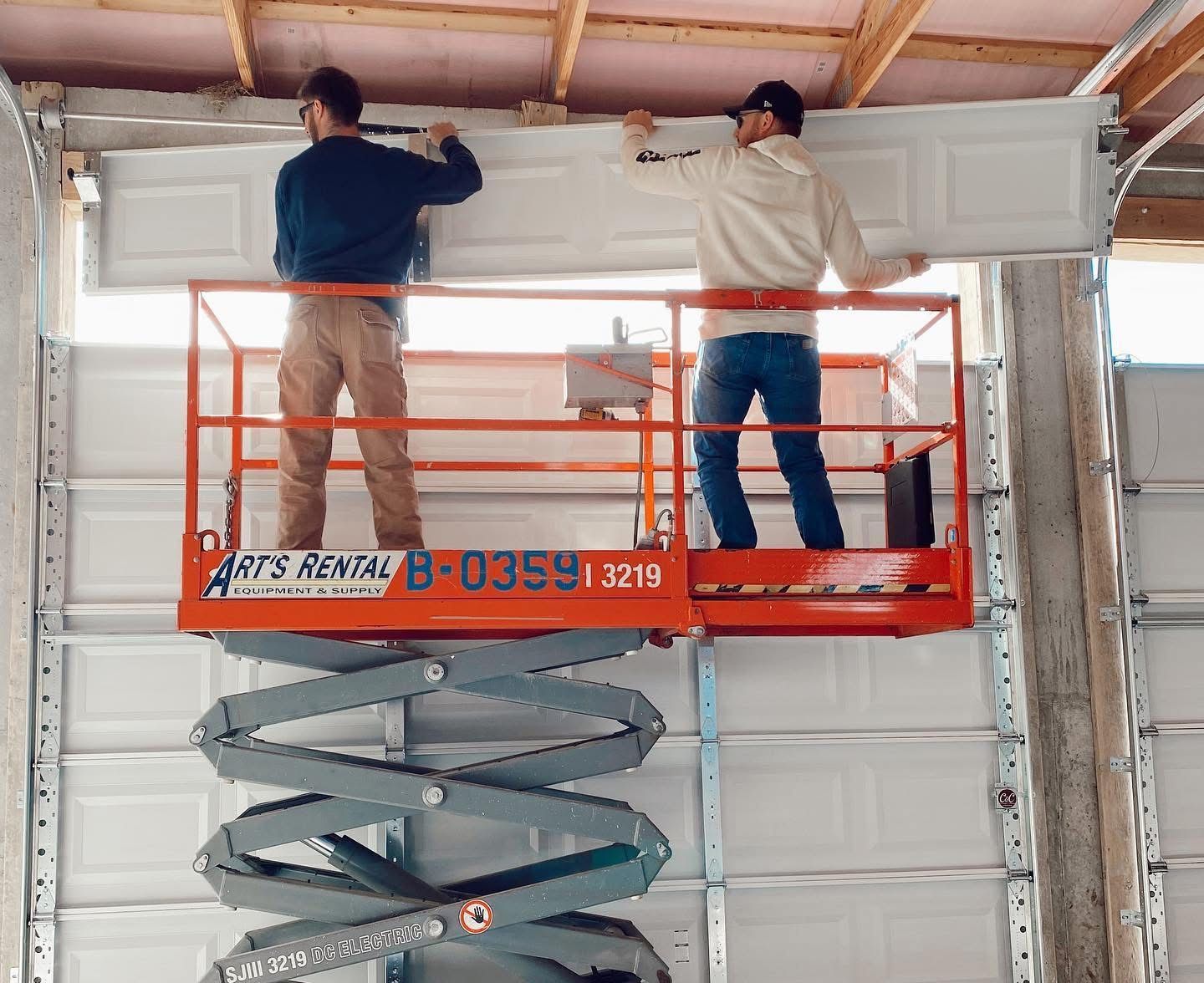 Two men are working on a garage door on a scissor lift