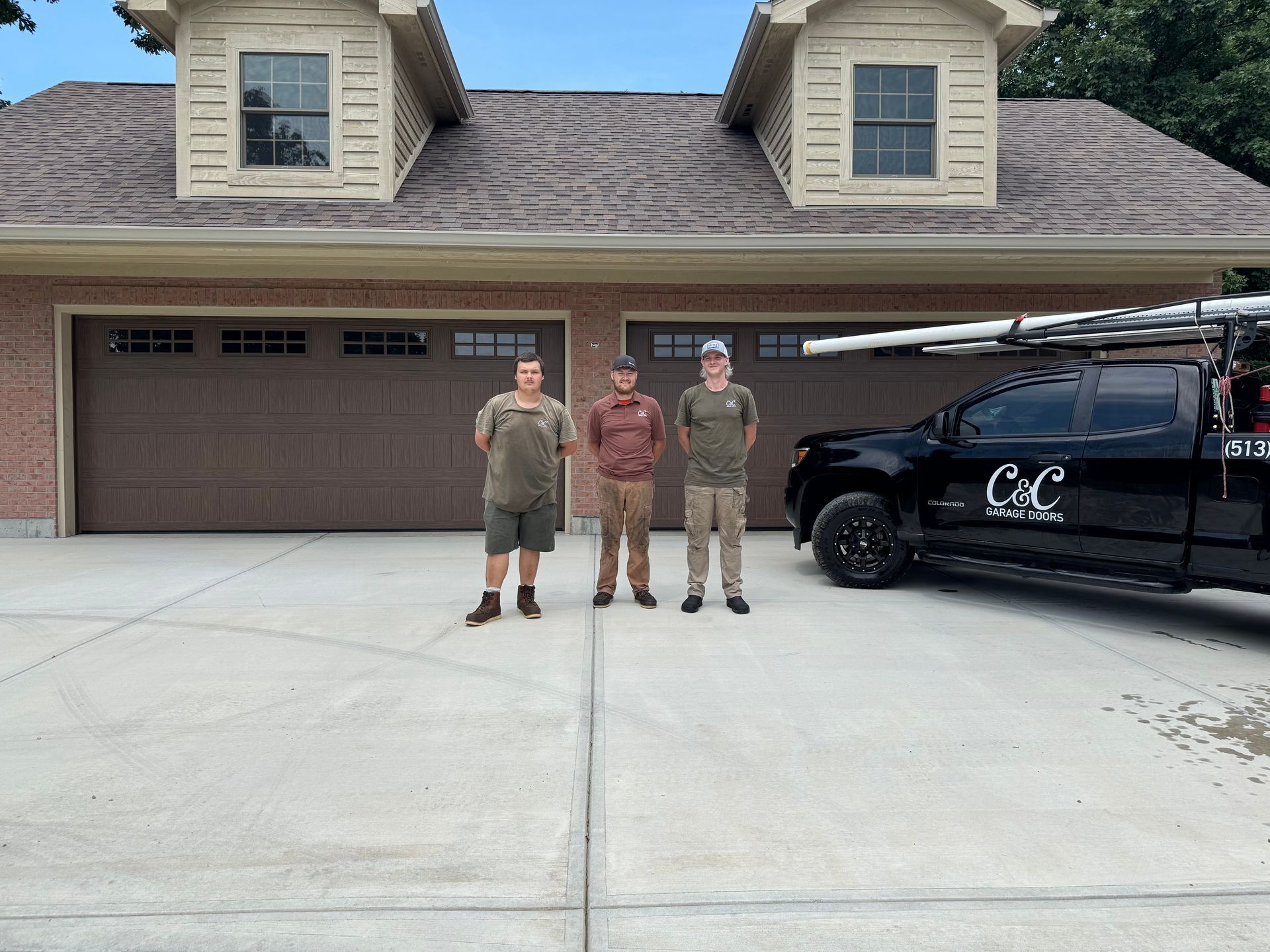 Three men are standing in front of a garage next to a truck.