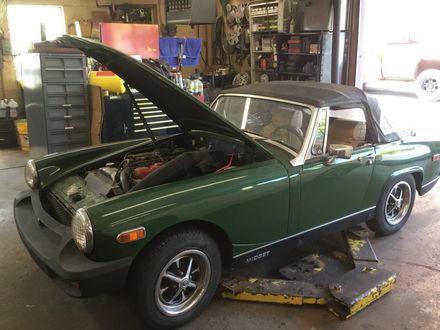 A green sports car with the hood up is parked in a garage.