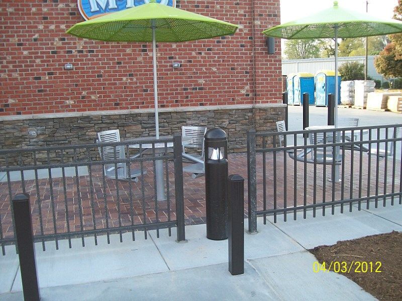 A fenced in area with tables and umbrellas in front of a brick building