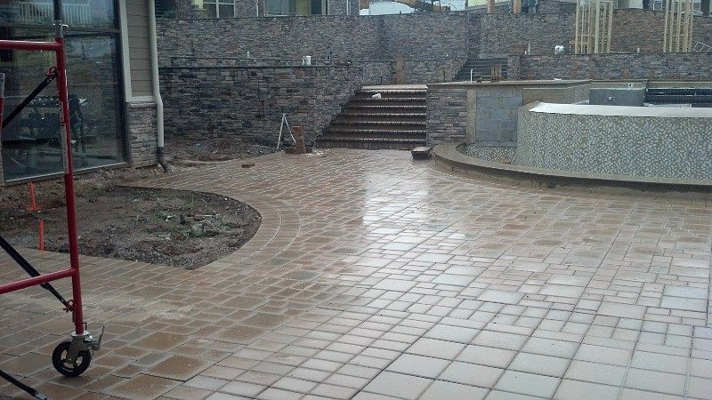 A brick patio with a scaffolding in the foreground and a pool in the background.