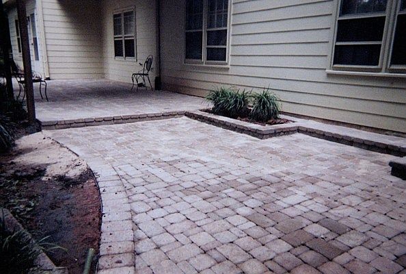 A brick patio with a bench in the middle of it in front of a house.