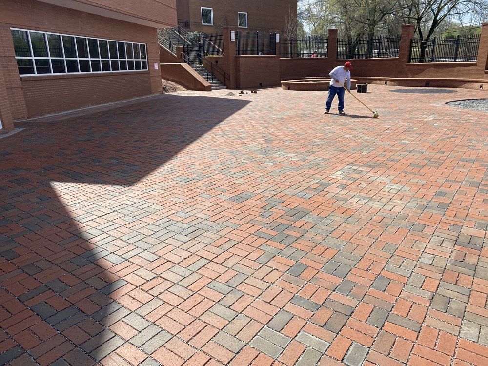 A man is sweeping a brick driveway with a broom.