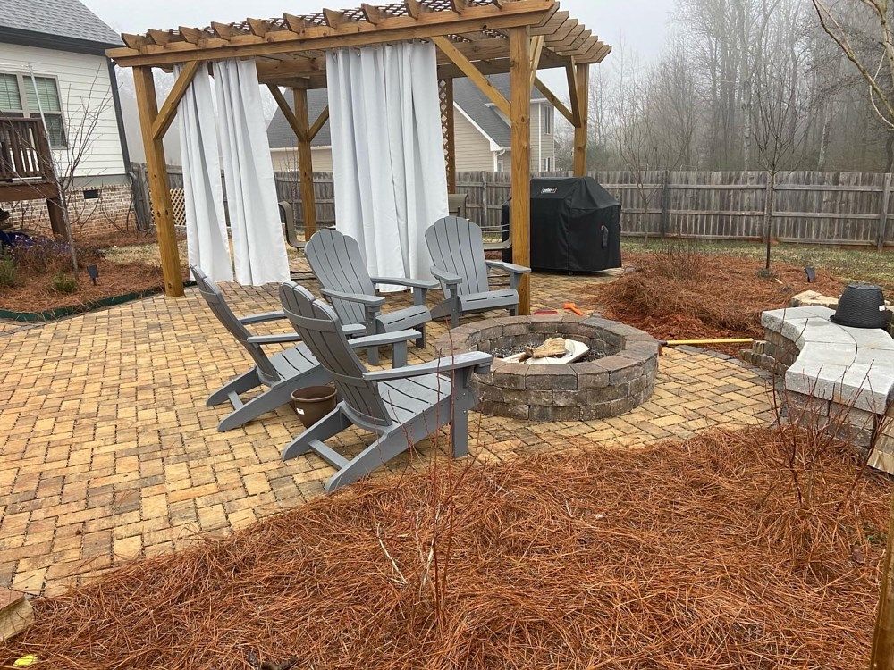 A patio with a fire pit and chairs under a pergola.