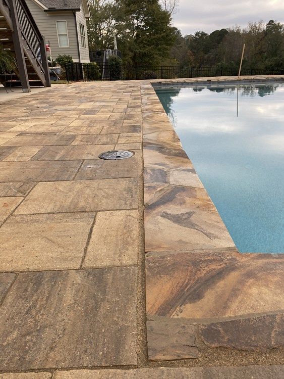 A swimming pool with a brick patio and a house in the background.