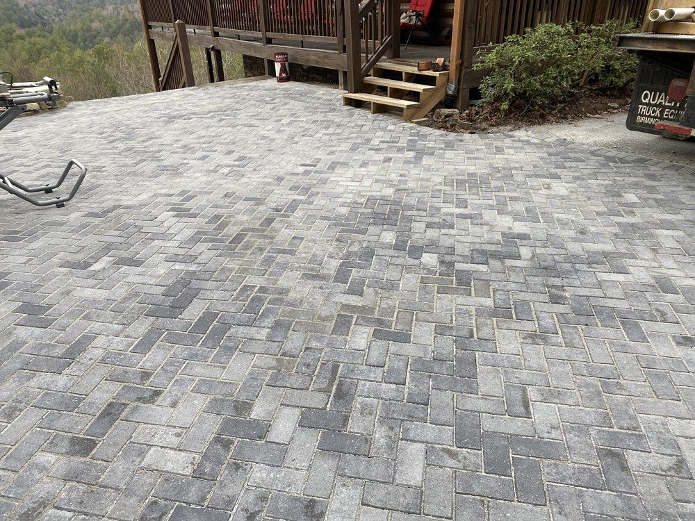 A brick driveway leading to a house with a deck.