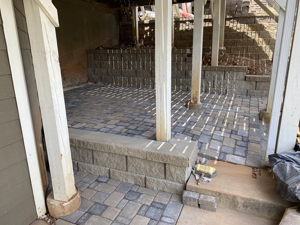 A brick walkway is being built under a covered porch.