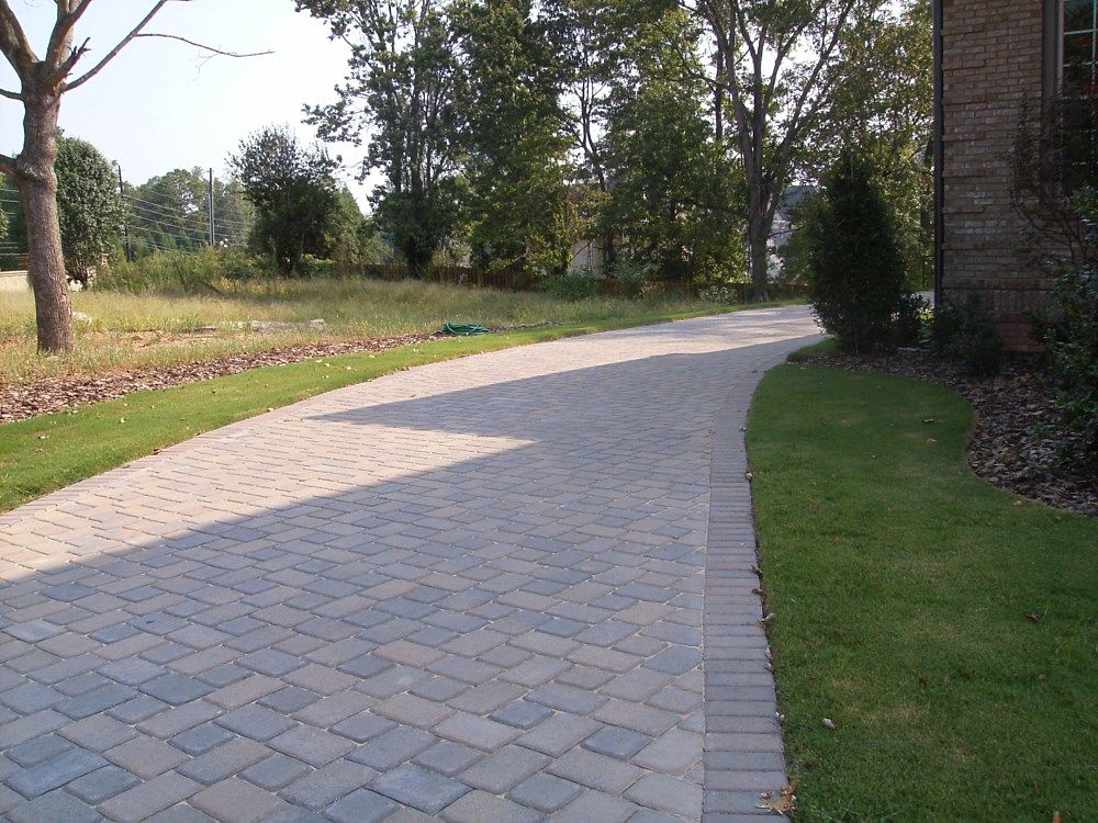 A brick driveway leading to a house with trees in the background
