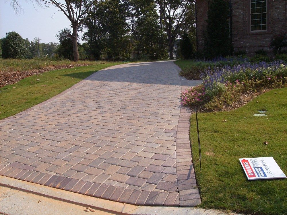 A brick driveway leading to a house with a for sale sign on the grass