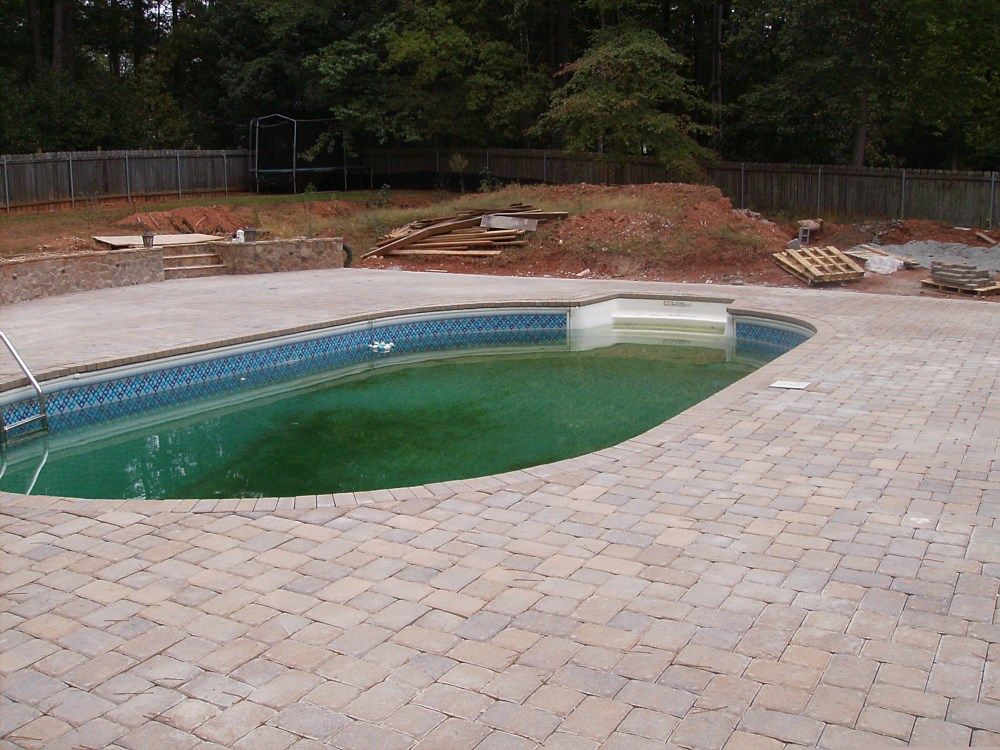 A swimming pool with green water and a brick patio