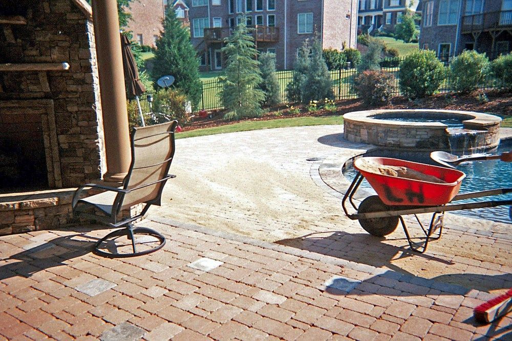 A wheelbarrow is sitting on a brick patio next to a chair.