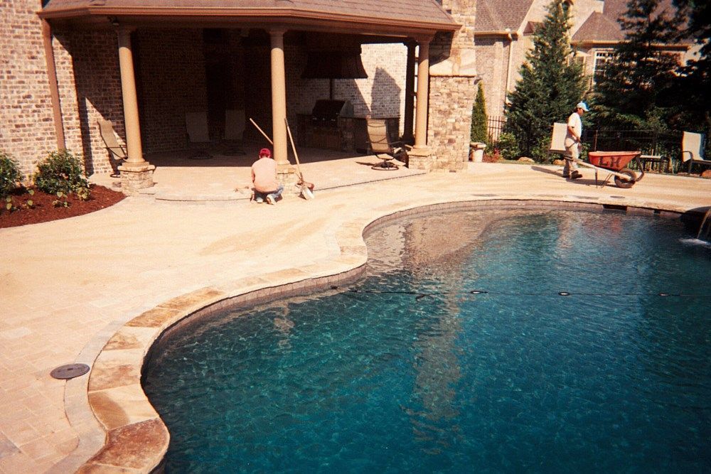 A man is kneeling next to a large swimming pool