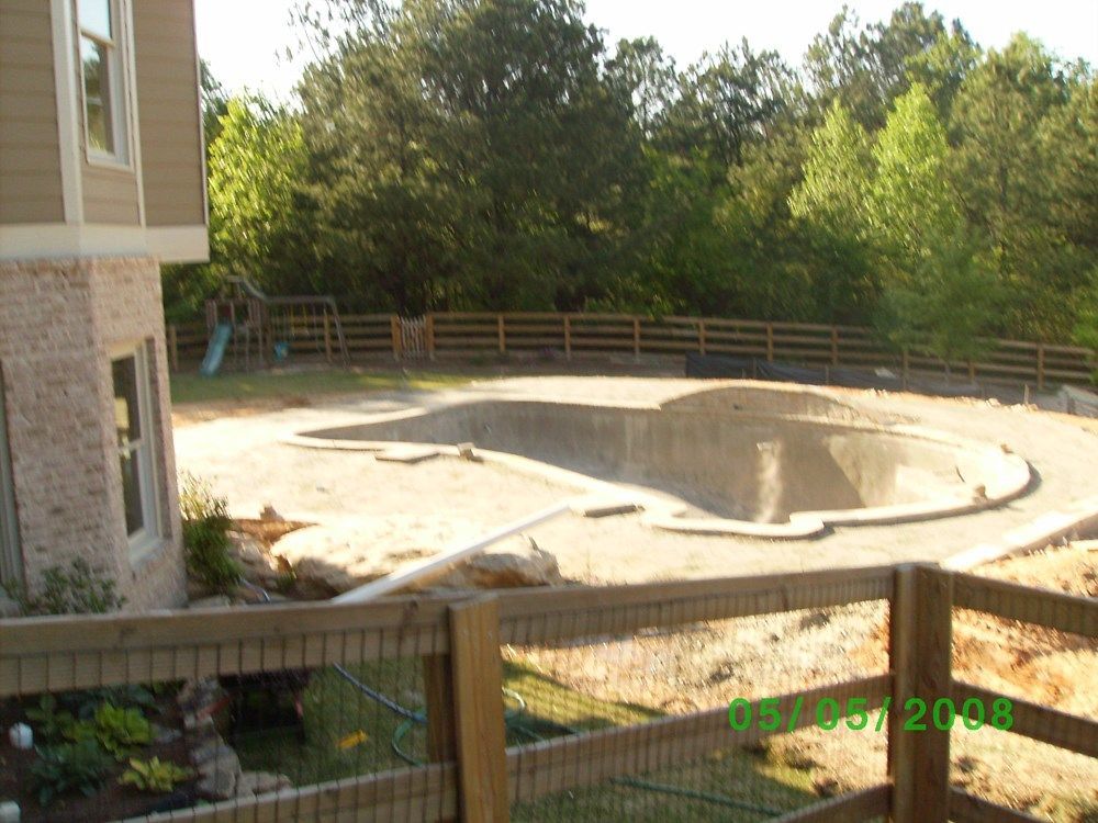 A wooden fence surrounds a swimming pool that is being built