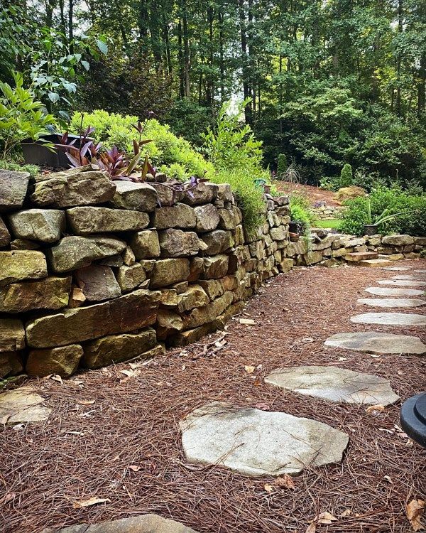 A stone wall with stepping stones leading to it in a garden.
