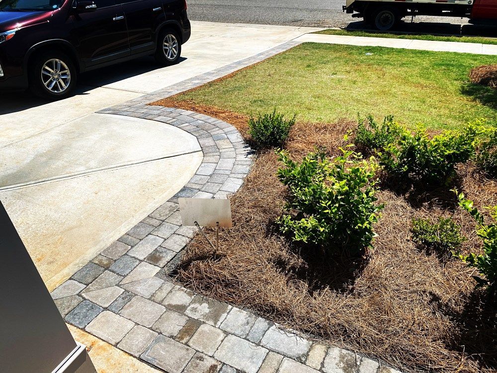 A car is parked in a driveway next to a brick walkway.