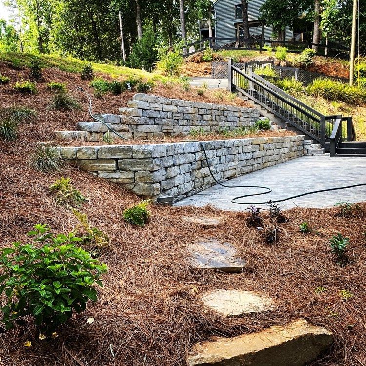 A stone wall with stairs leading up to a patio and a house in the background.