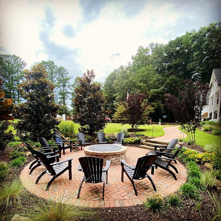 A fire pit surrounded by chairs and trees in a backyard.