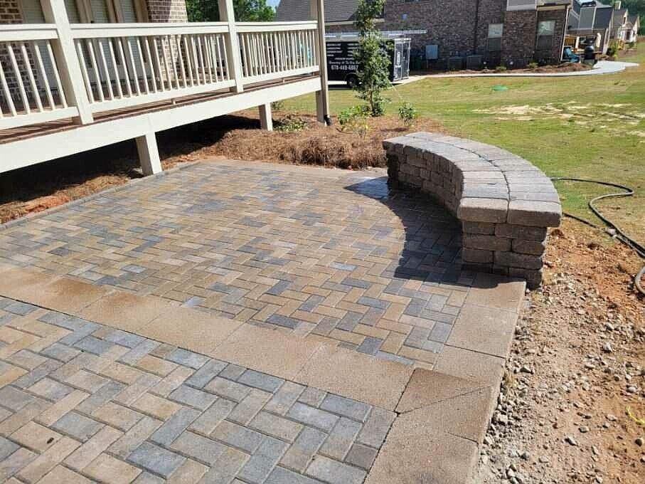 A brick patio with a bench and a deck in the background.