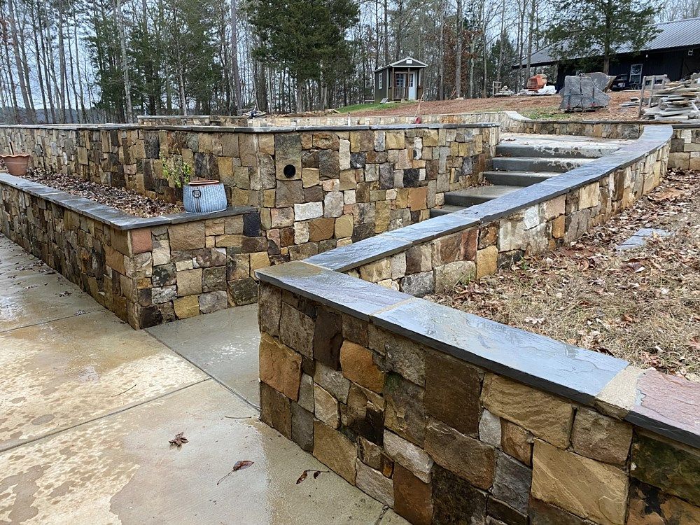 A stone wall with stairs leading to a house in the background.