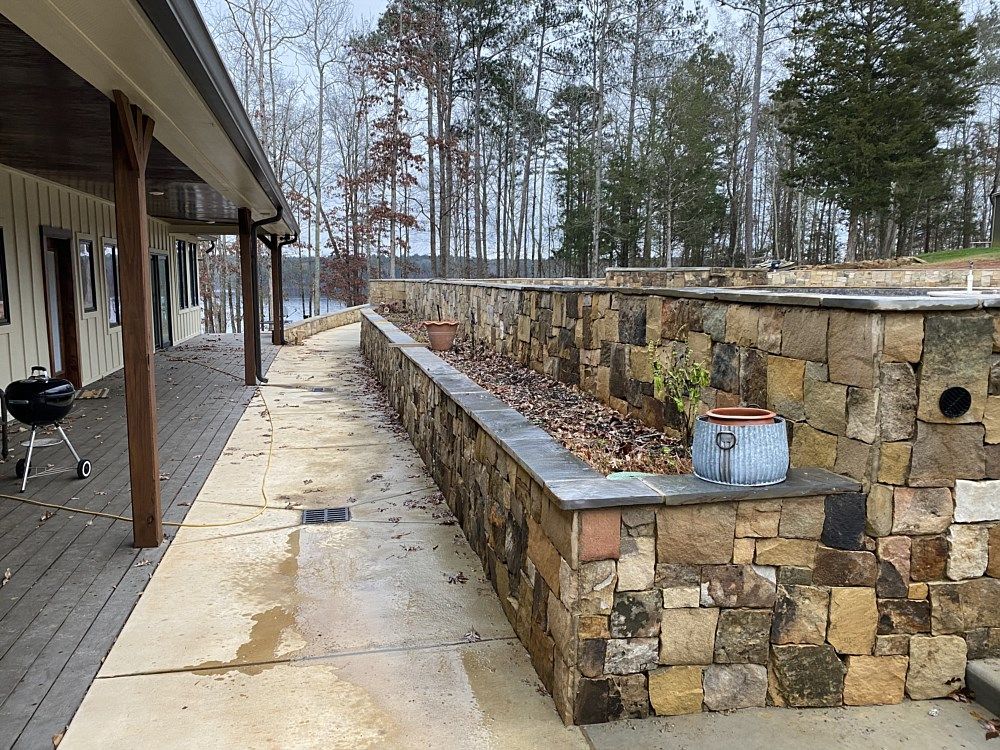 A stone wall with a potted plant on top of it next to a wooden deck.